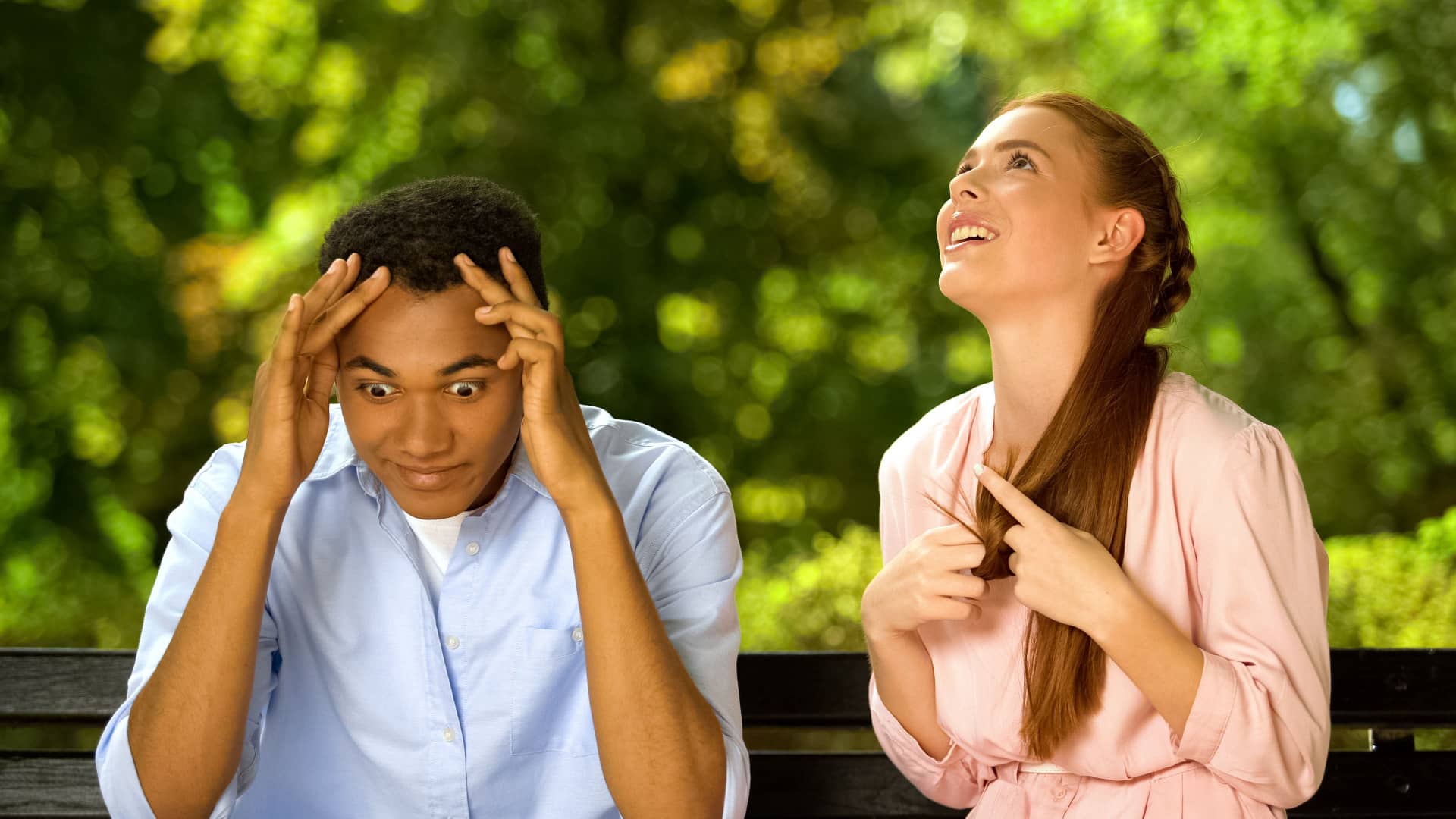 A man and woman sit on a bench. He's obviously annoyed, but she's oblivious and talking.