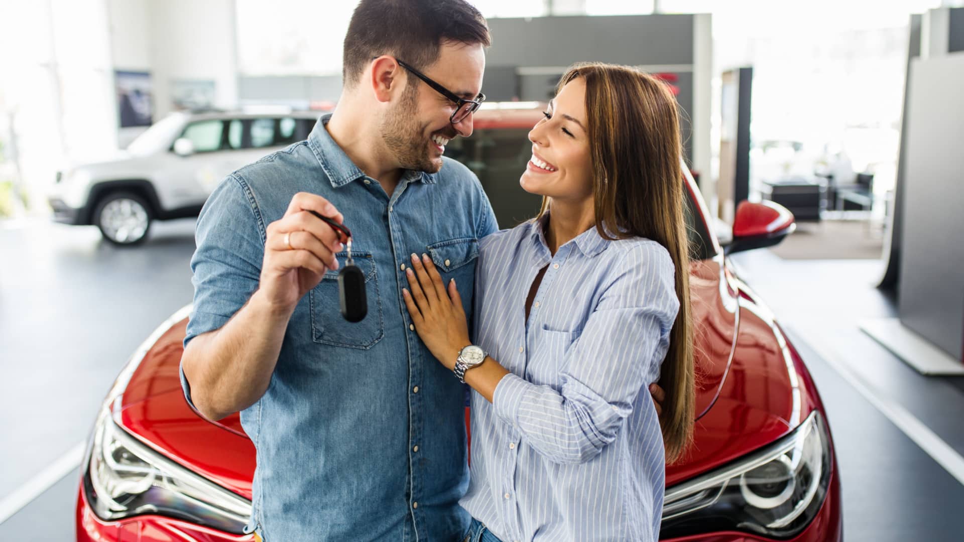 A couple stands happily in front of a car, holding the keys as if they just bought it.