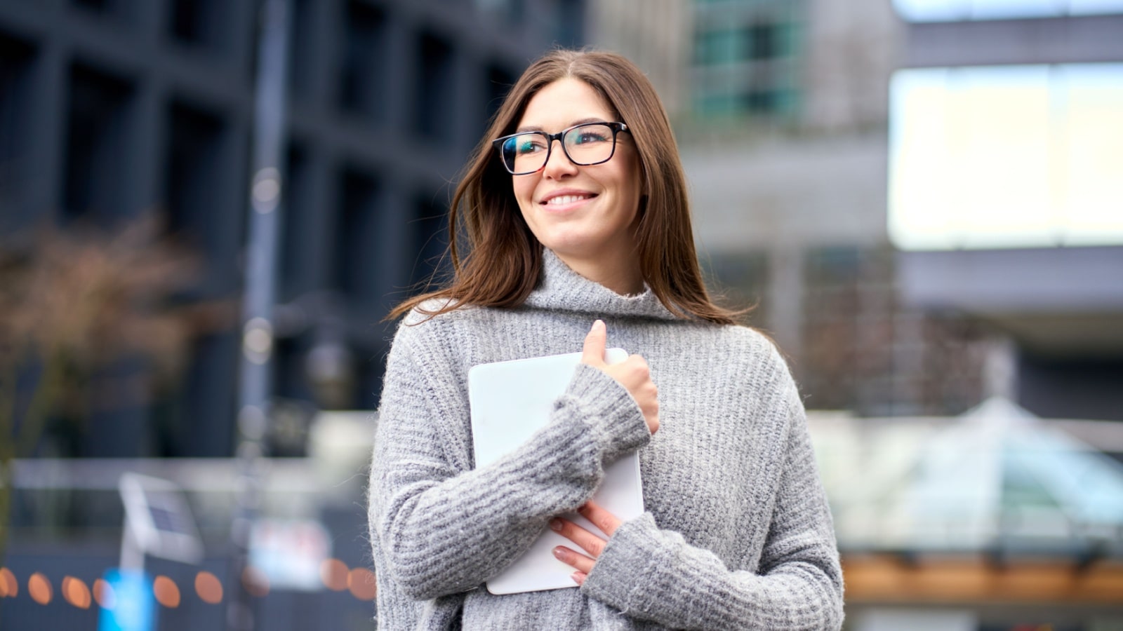 A confident looking woman hugs her tablet, and smiles, looking forward to life's possibilities.
