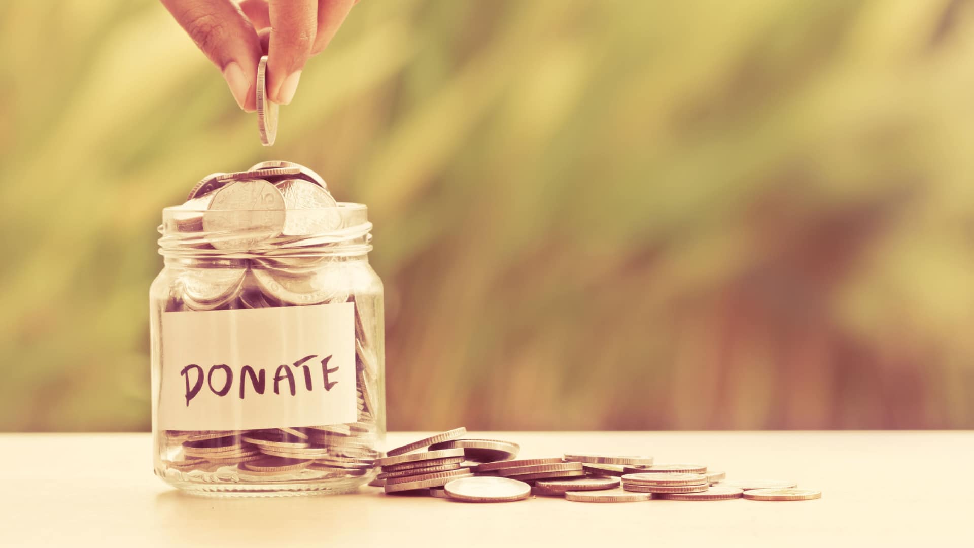 Fingers dropping coins in a donation jar.