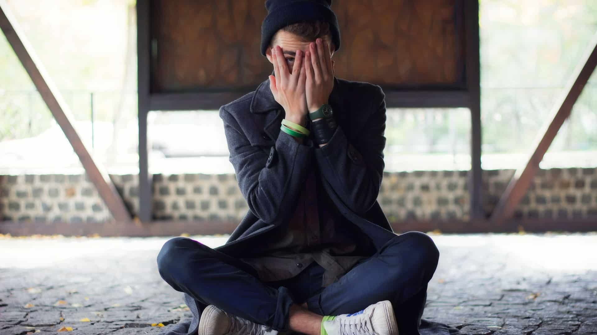 teenager sitting on the ground covering his face in embarressment.