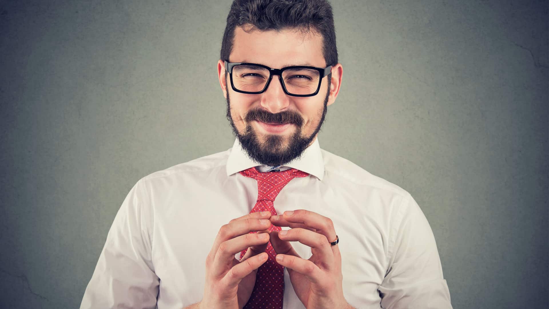 A salesman has his eyes squinted as if he's trying to pull a fast one, and his hands are near his chest with his fingertips slighlty touching.