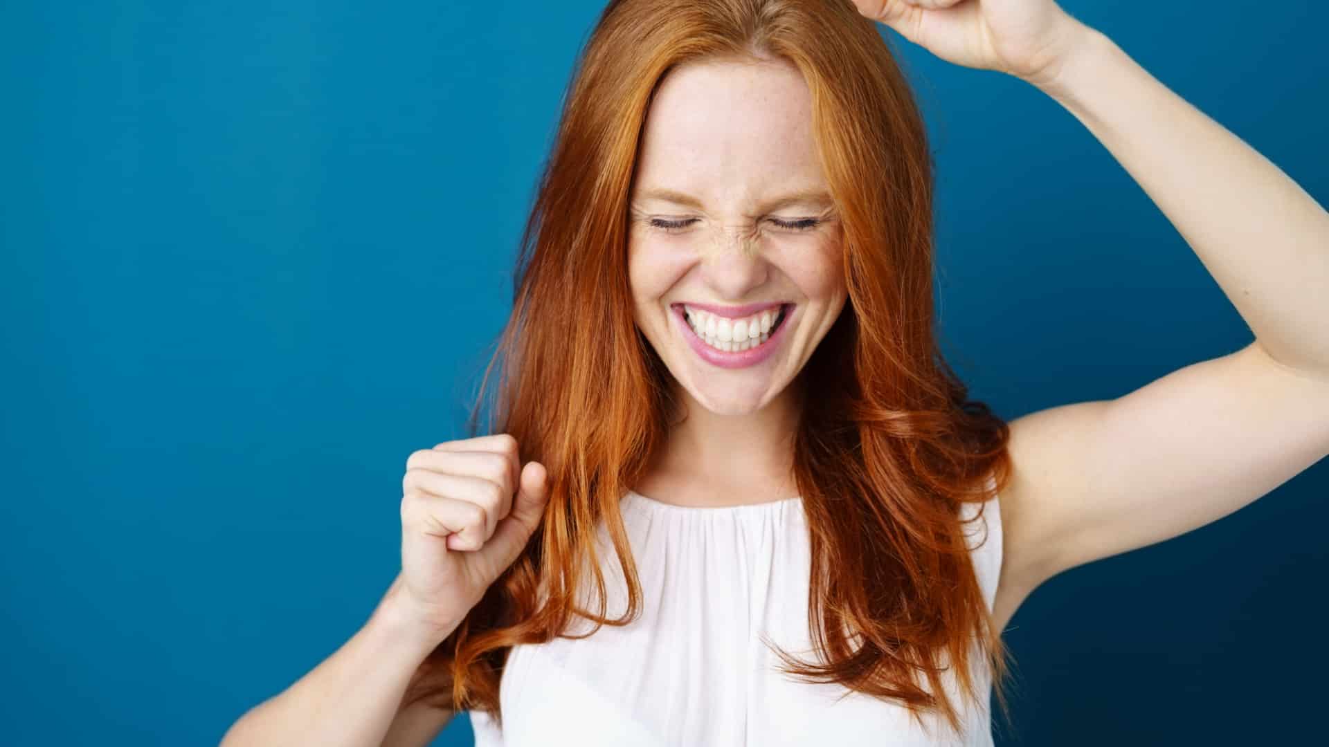 A happy woman with her arms up as if she just won big and a giant smile on her face.