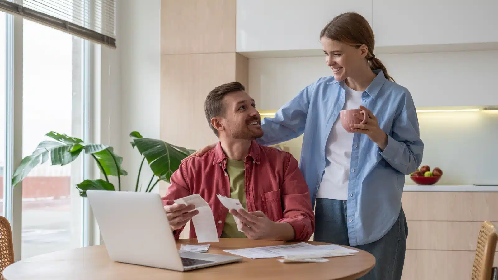 A happy couple reviews their bills and receipts, representing how to save money on living expenses.