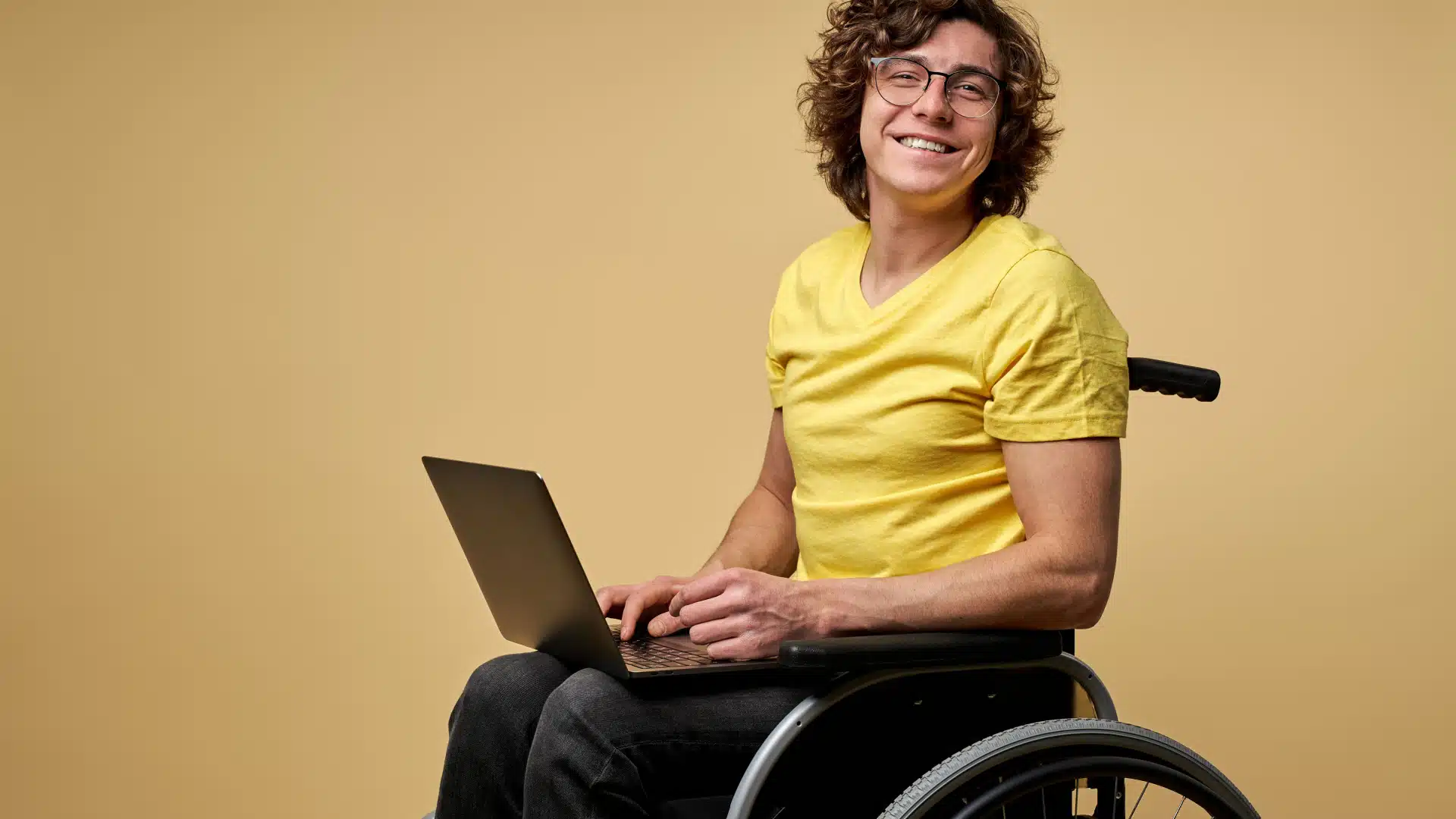 A man sits in a wheelchair with a laptop on his lap.  He turned to the camera and smiled.