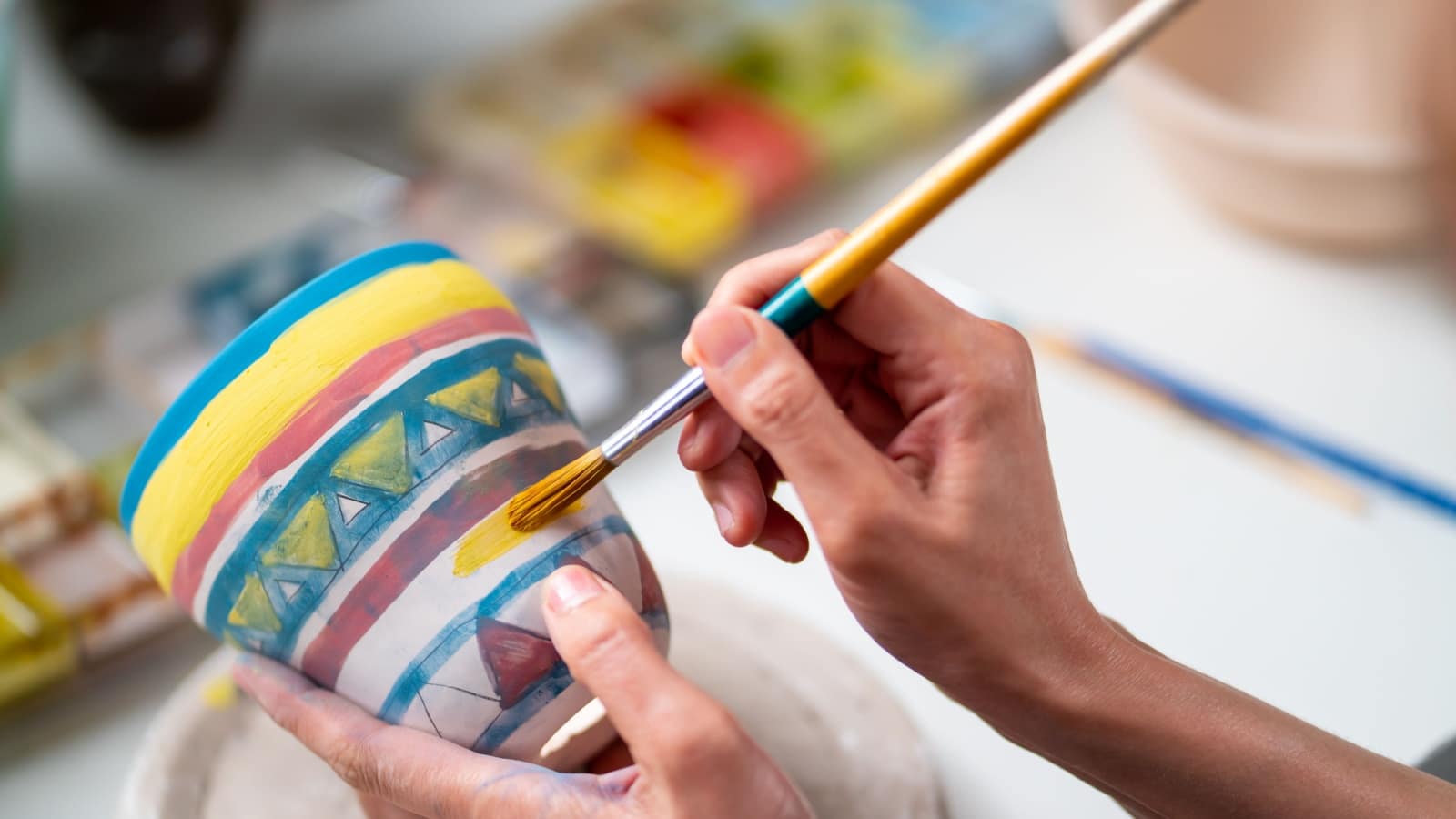 Woman painting a small ceramic vase she created.