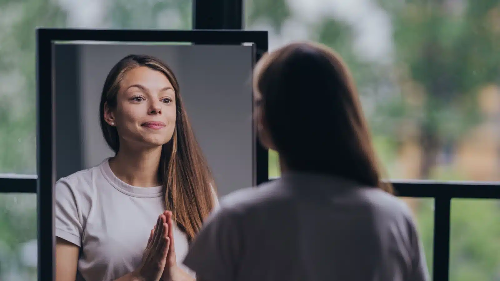 A woman looks at herself in the mirror, setting positive affirmations with positive self talk.