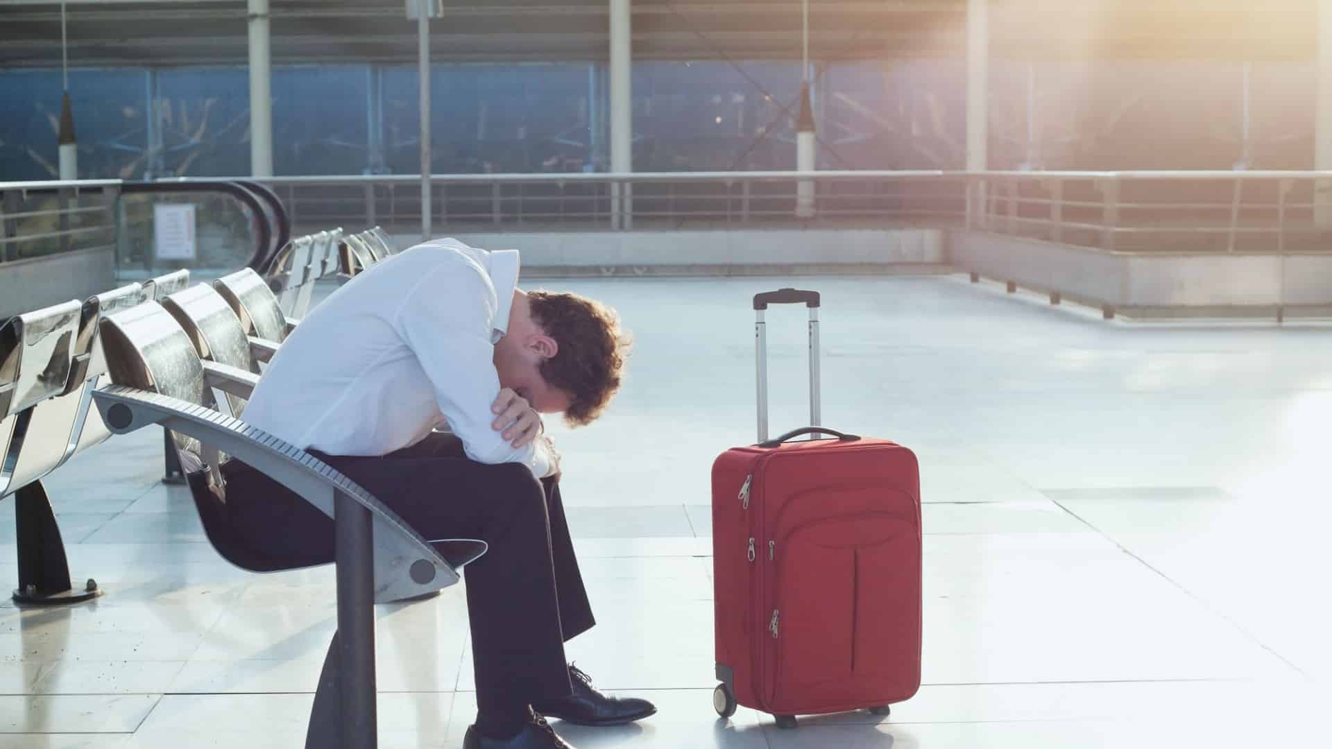 A man sits alone in an airport terminal burying his head in he lap.