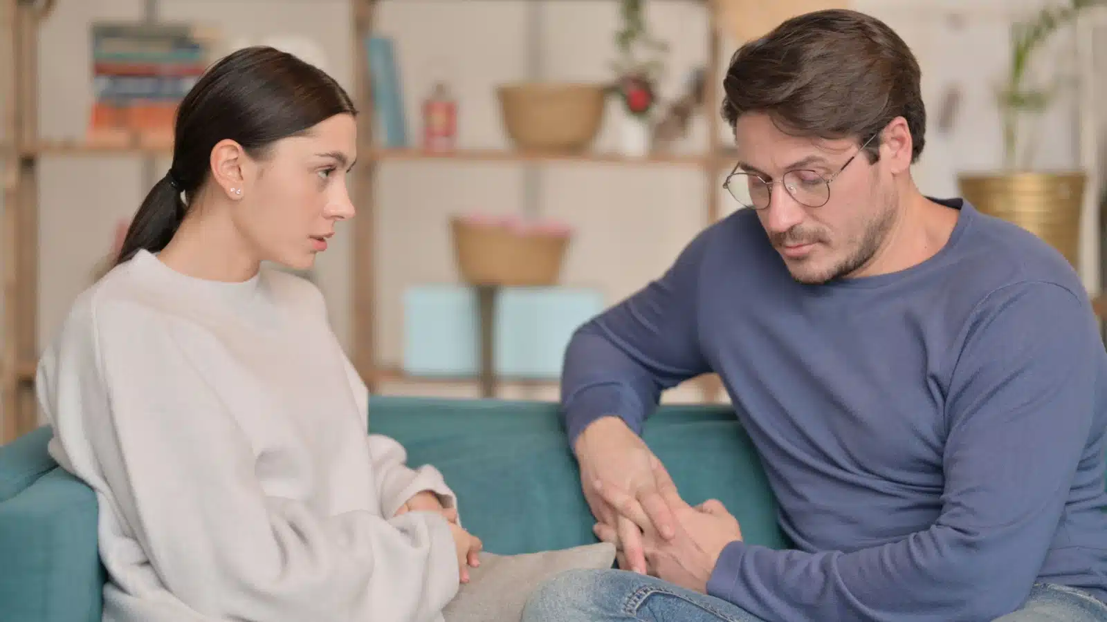 A couple sits on the couch, holding tension after a fight.