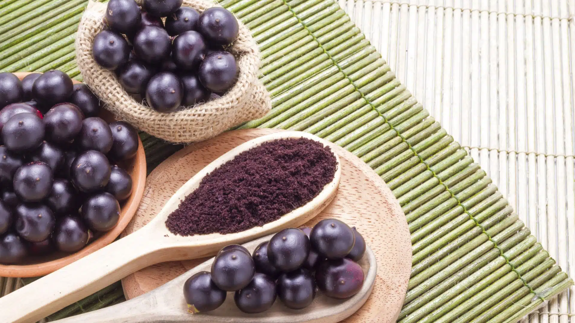 Fresh acai berries and some acai powder in a wooden spoon. 