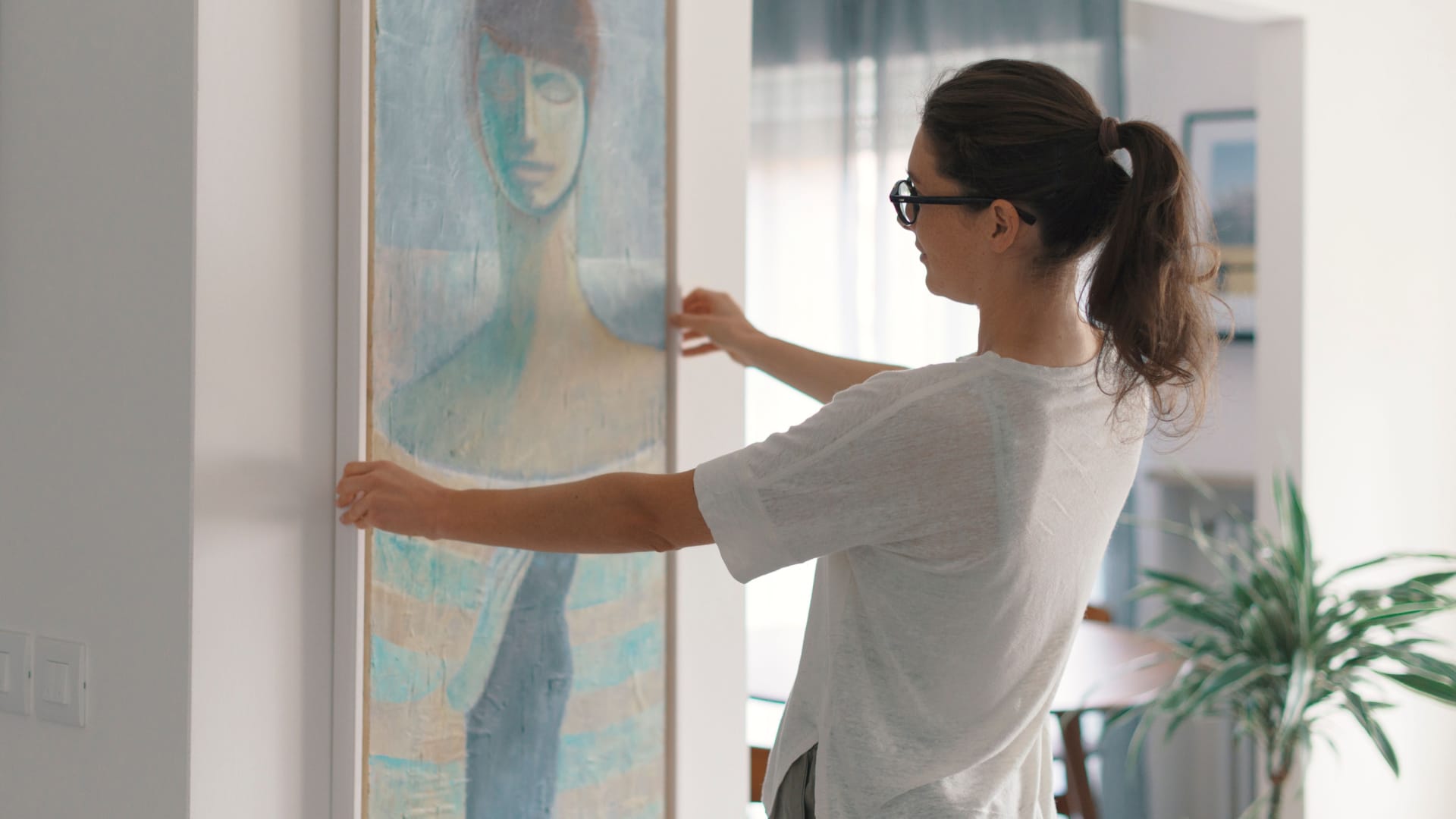 a woman adjusting a framed painting on a wall.