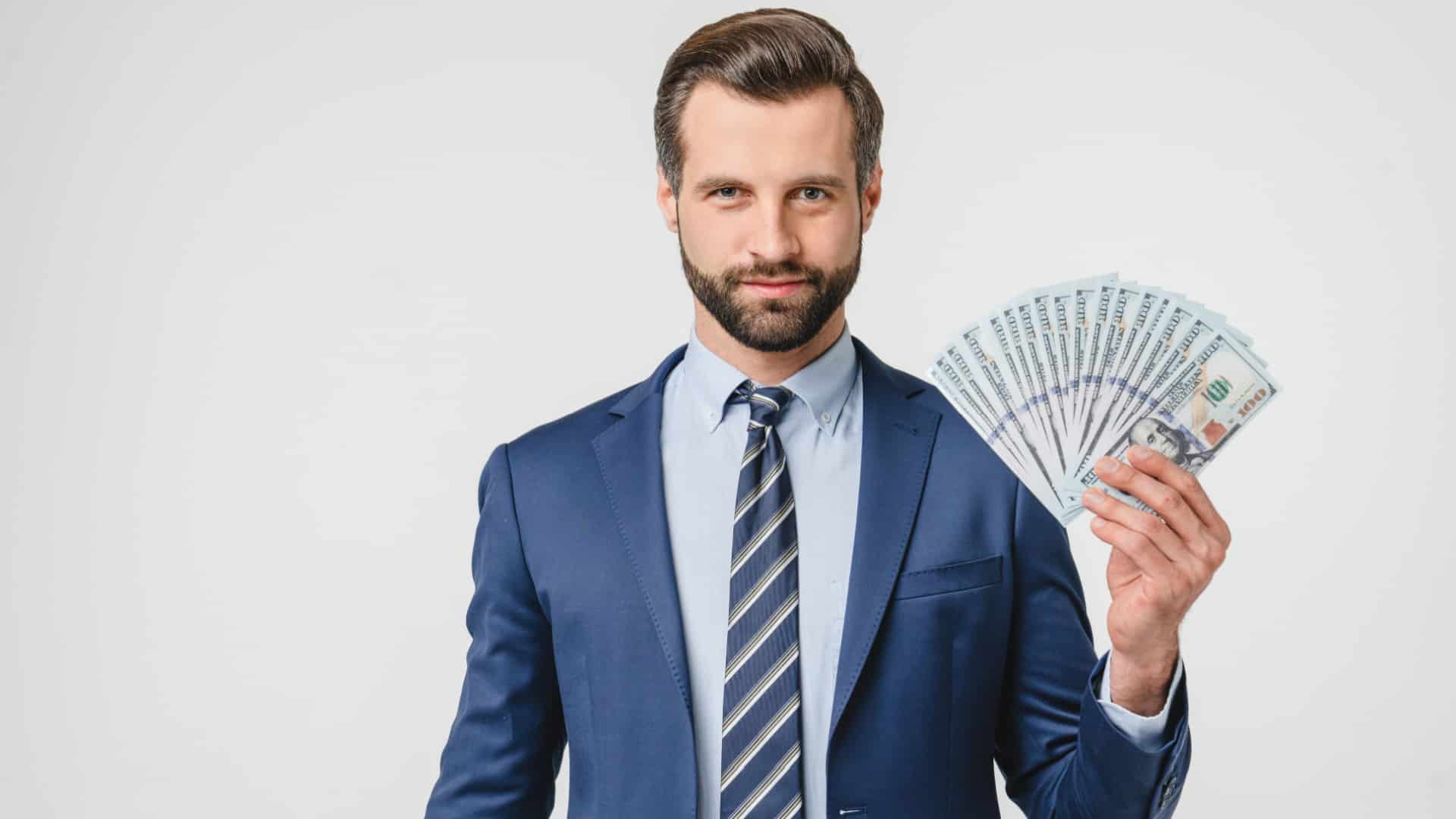 A business man in a suit holding up a large stack of money.