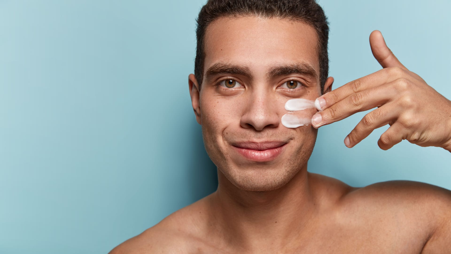 A man rubbing skin care lotion under his eye.
