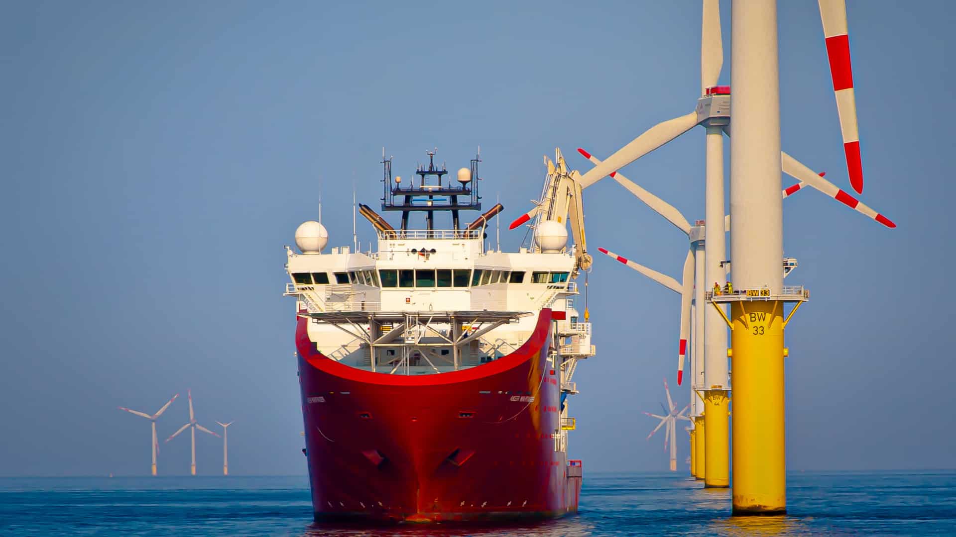 A large industrial vessel that looks like a tanker on the ocean next to giant windmills.