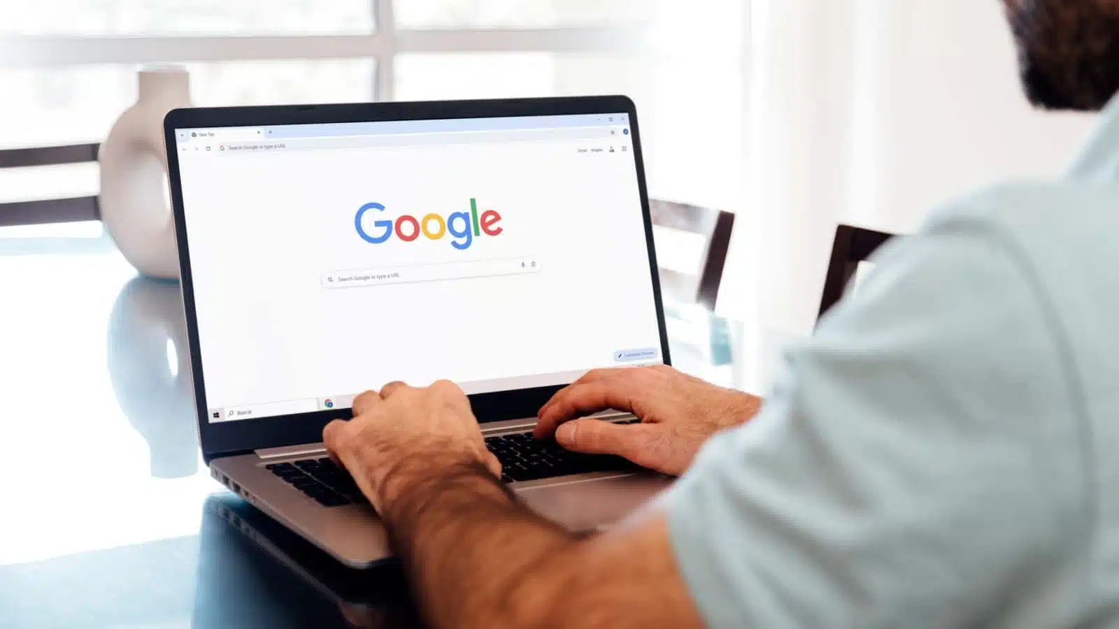 A man using a laptop open to the Google search home page. 