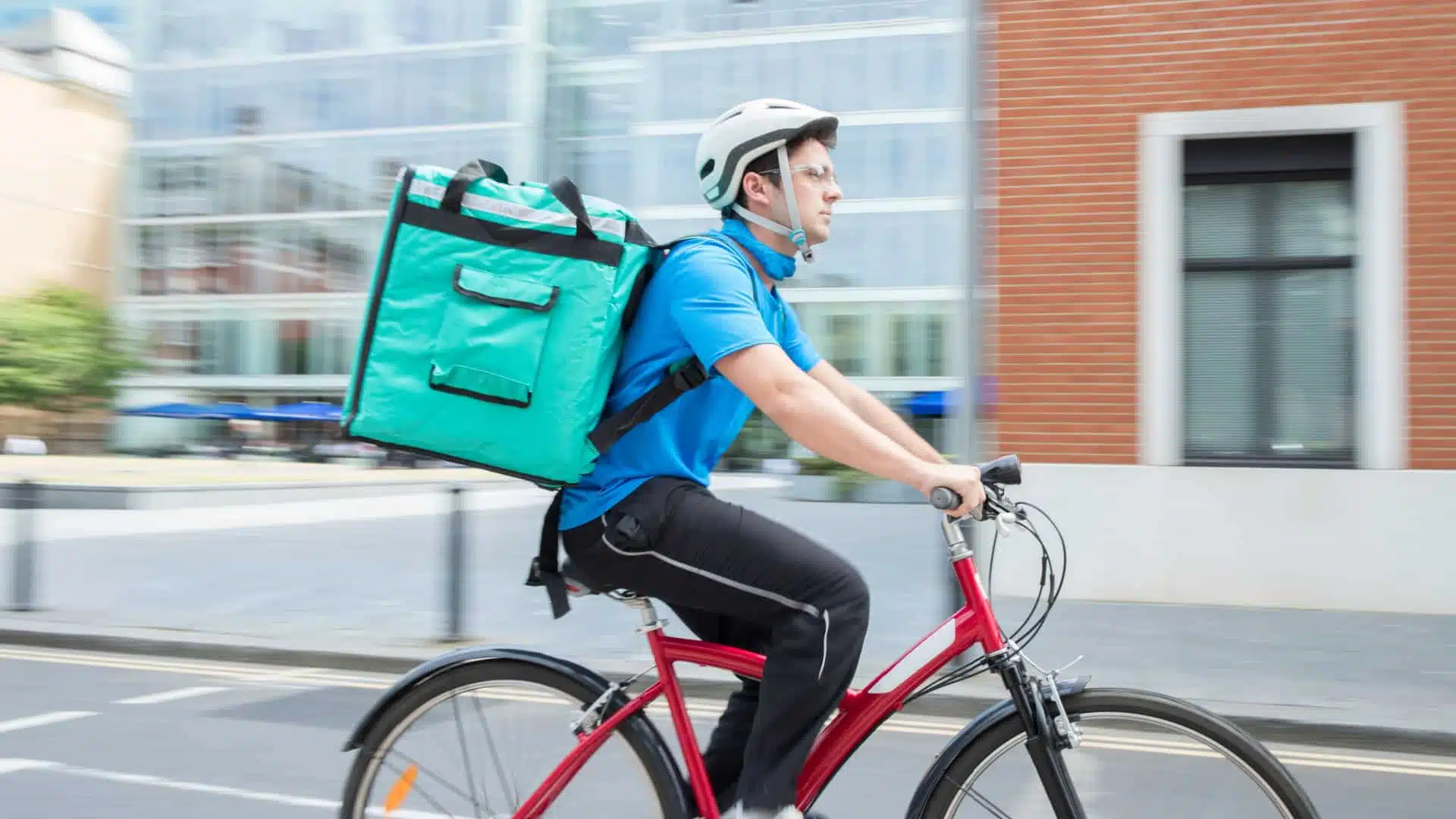 A man riding a bicycle with a food delivery bag on his back. 