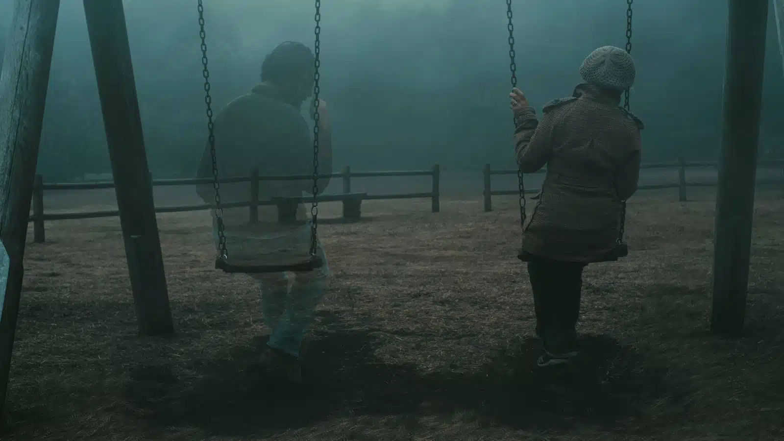 A man's ghost sitting on the swing set next to a living woman, to represent the question "are ghosts real?"