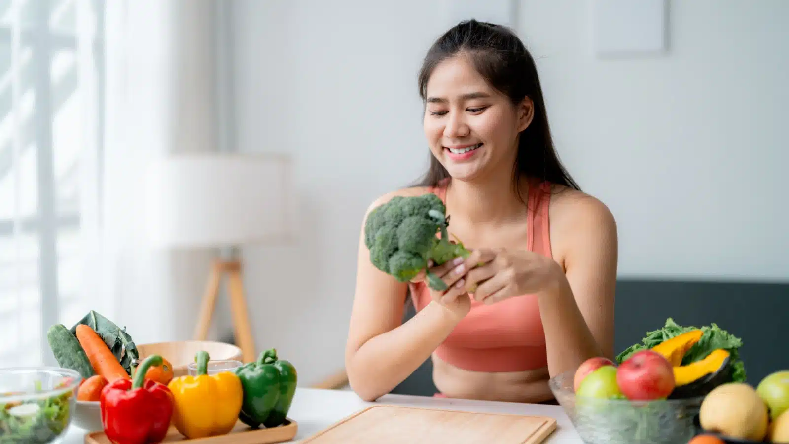 A healthy looking woman holds a fresh stalk of broccoli as she gets ready to prepare a meal of fresh vegetables.