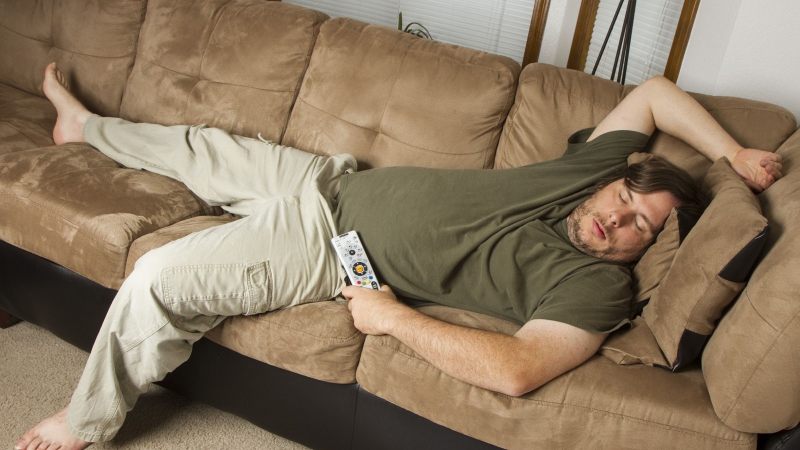 A lazy men fell asleep on the couch watching television.