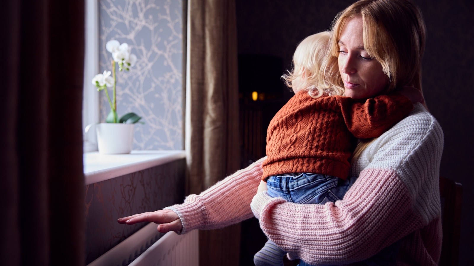 A mother hold her son near the radiator trying to keep warm.