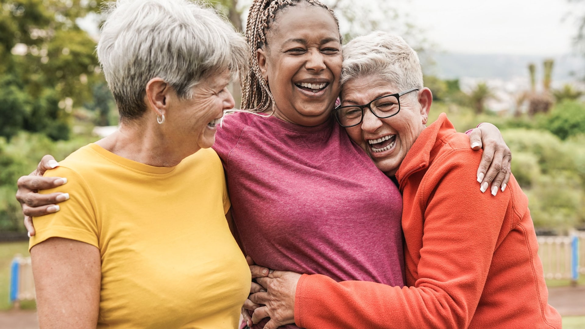 Three senior women happily embrace each other in friendship.
