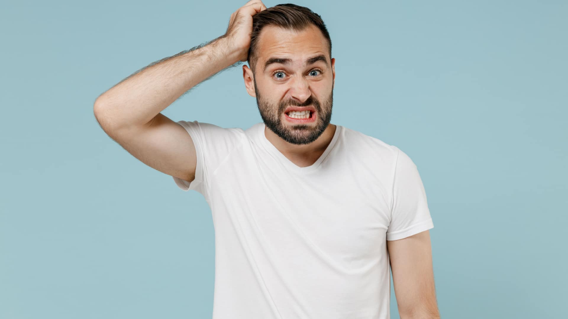 An unsure confused man wearing a white t-shirt scratching his head.