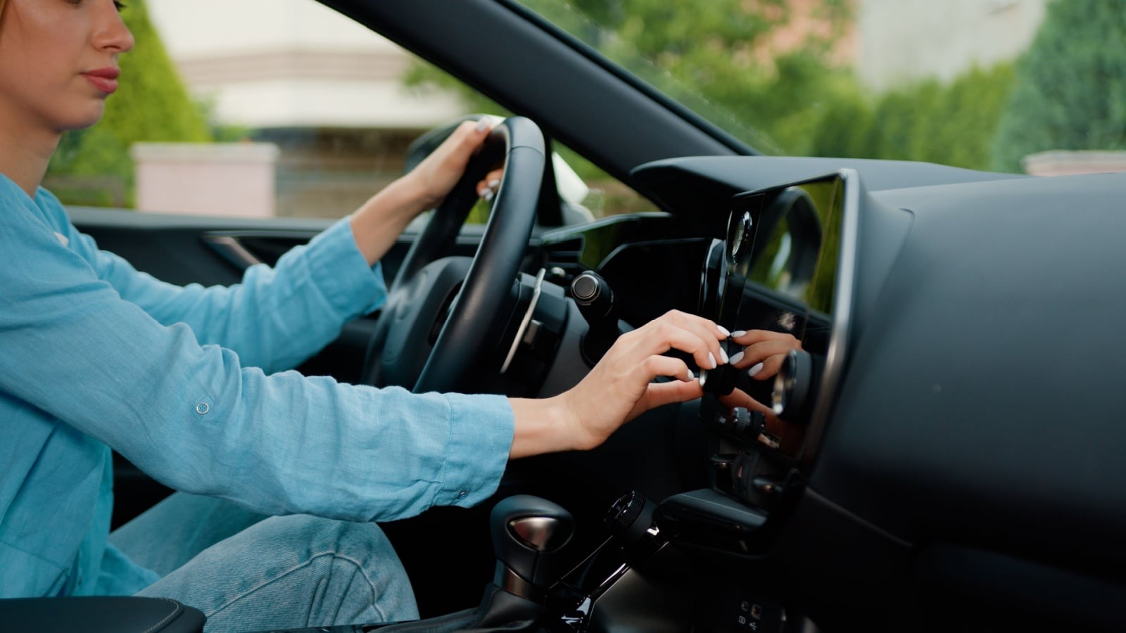 A woman driving while messing with her center console in the car.