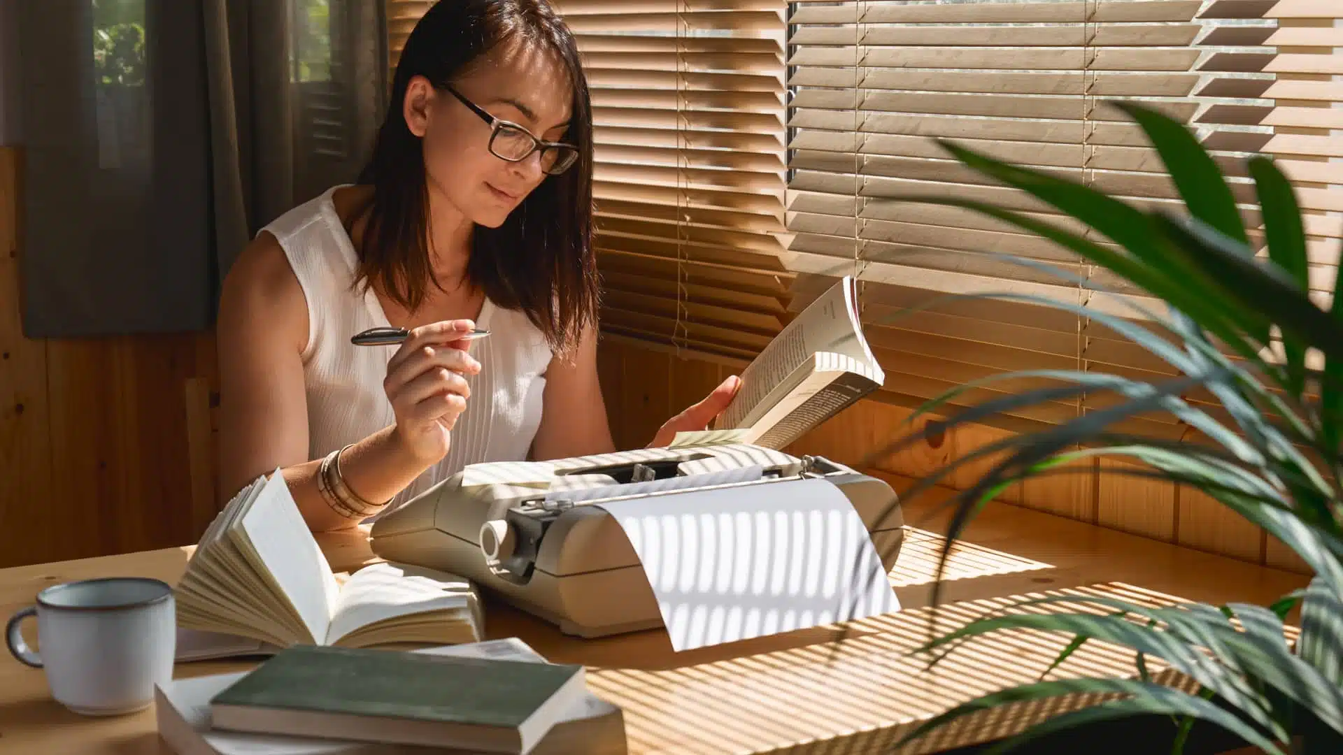 A woman sits at her desk and writes on an old typewriter.  She cross-references books for her work, which represents plot elements.