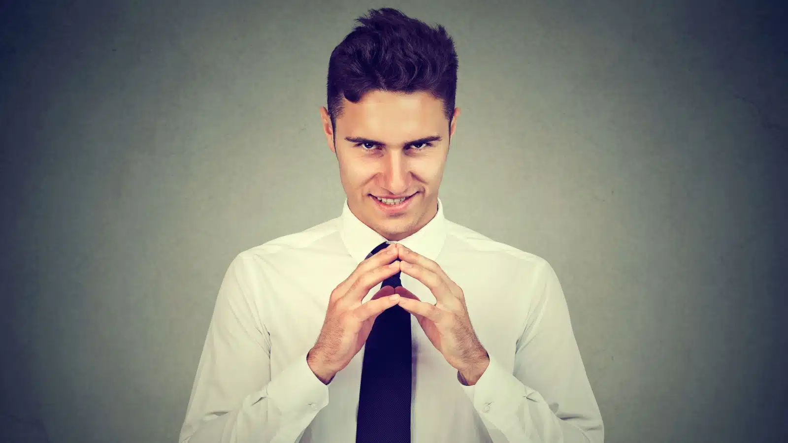 An evil looking man has his fingers together and looks as though he's cooking up a terrible scheme.