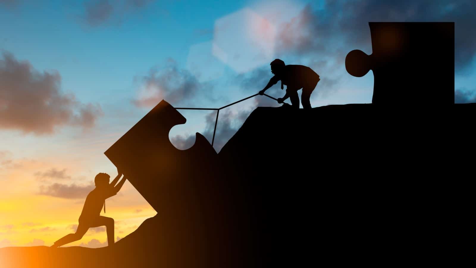 Silhouette of workers pulling a puzzle piece up a steep hill.