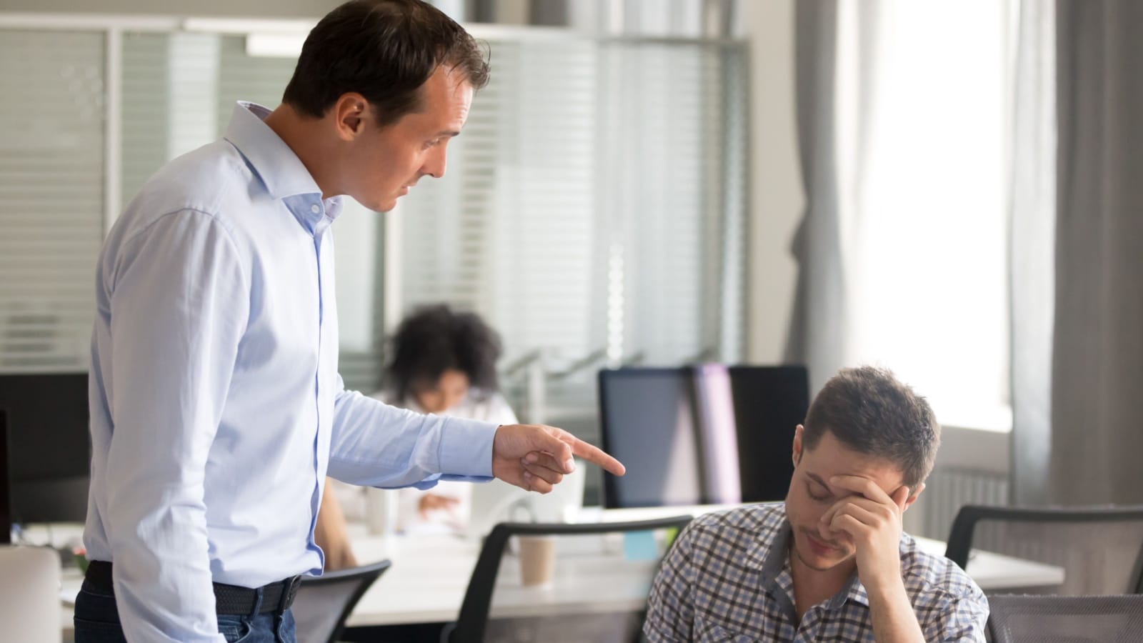 A boss stands over an employee, berating him.