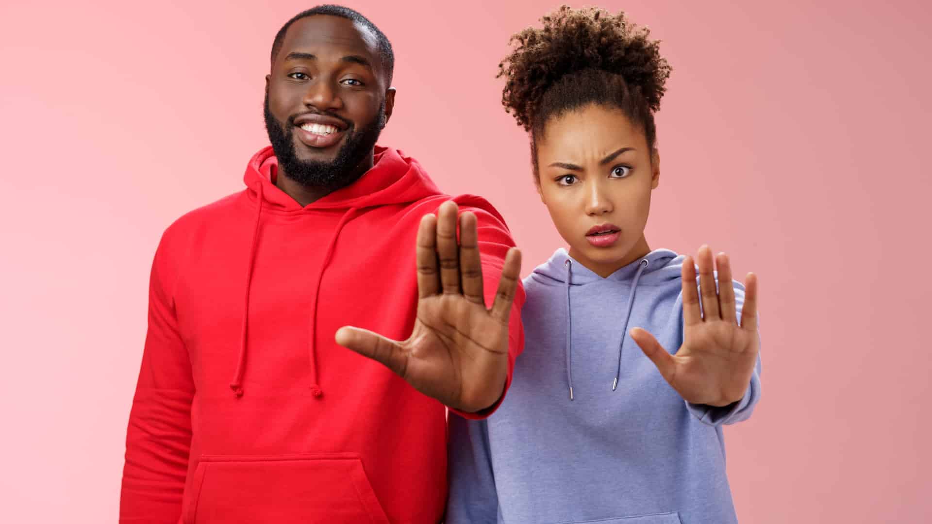 A man and woman stand next to each other, both have their hands out, palms up as if to say "stop."