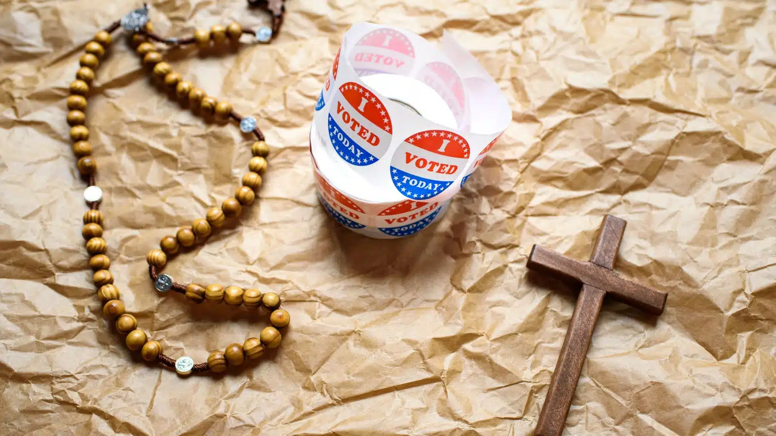 An "I voted" sticker rests between a cross and a rosary, to represent religion's influence in politics.