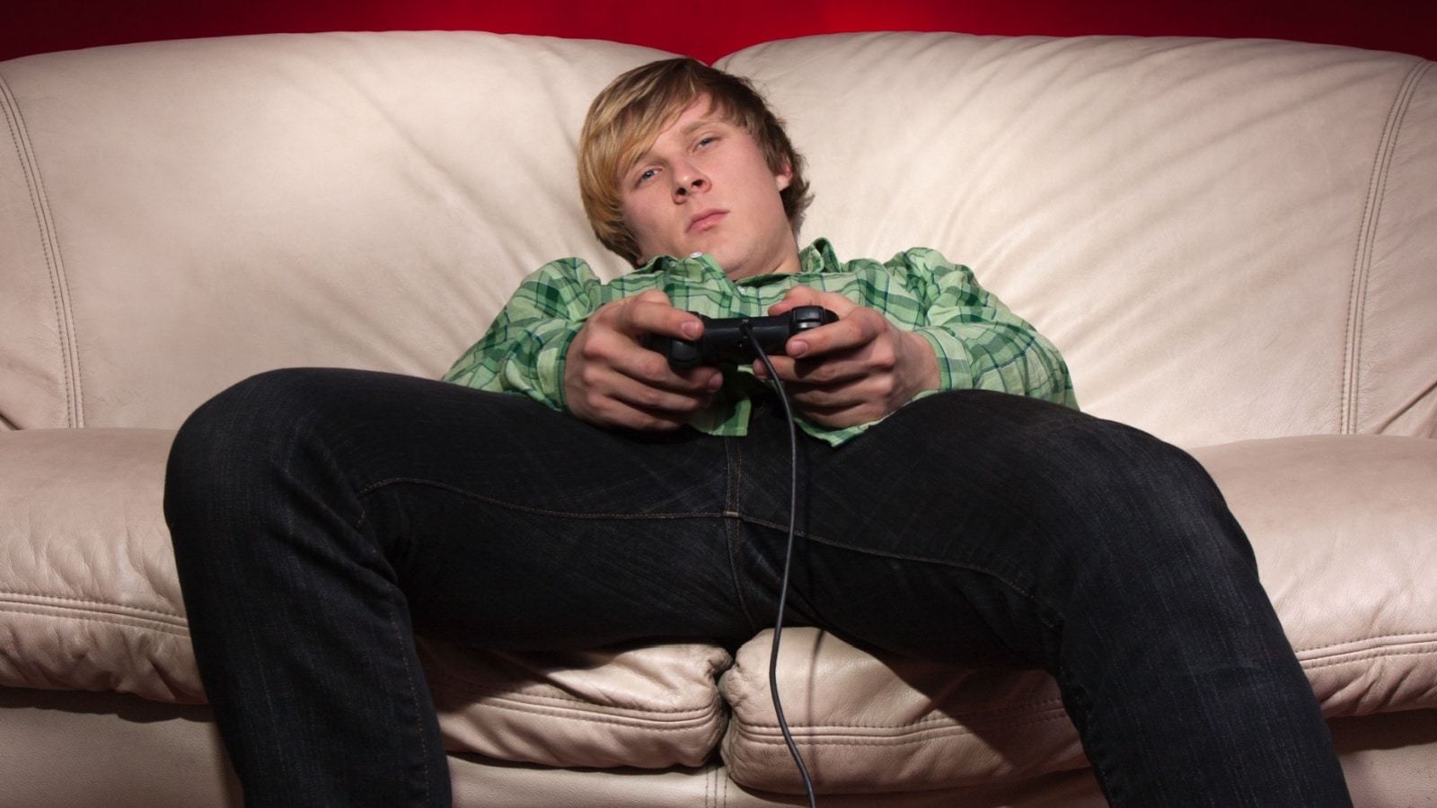 A man slumps on the couch holding a video game controller. He looks bored and alone.