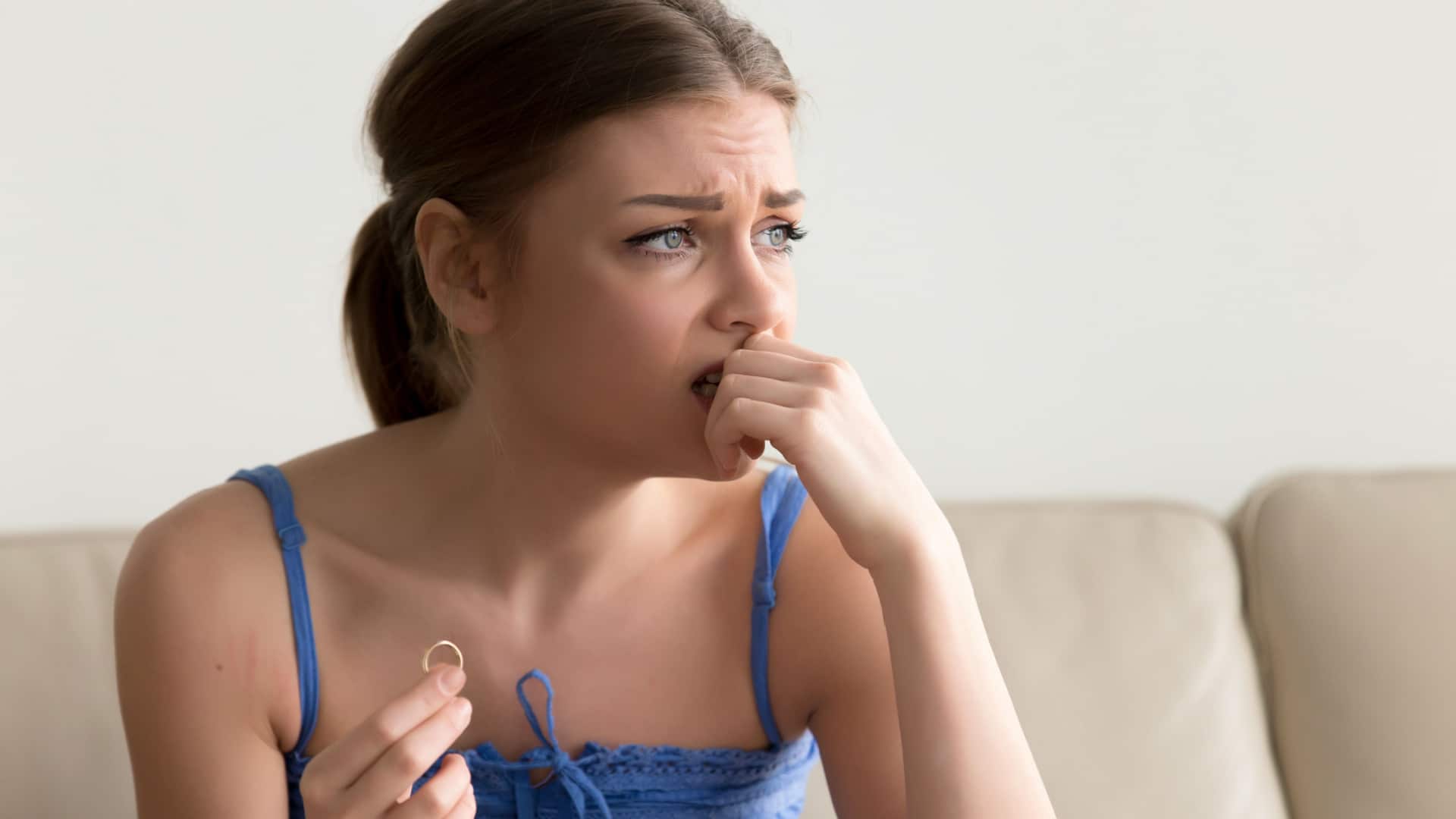 A sad unsure woman holds a wedding ring while pondering her future.