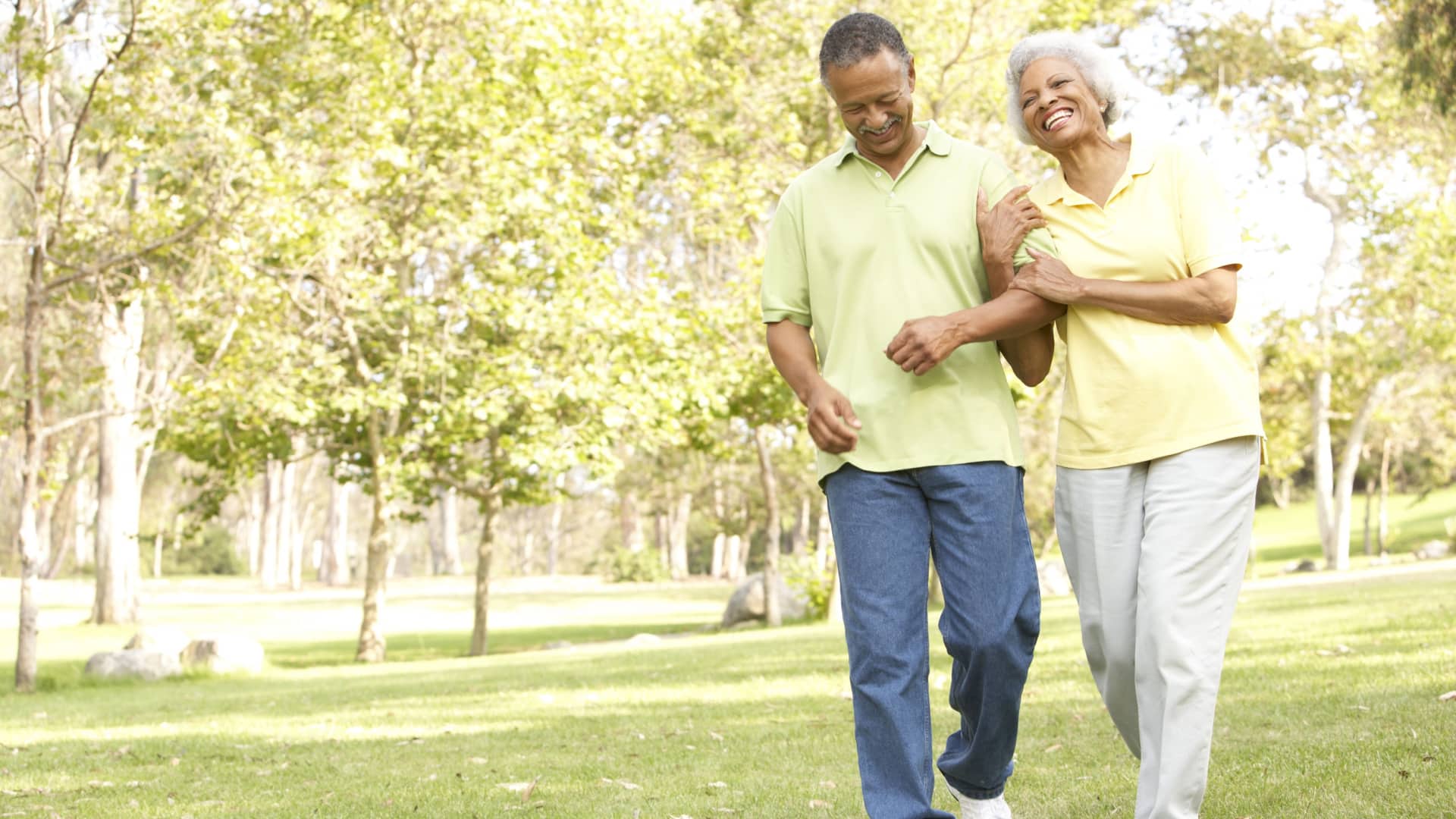 A senior couple walks happily through a park.