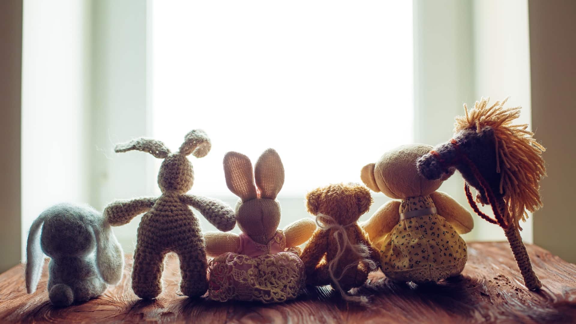 A line of small, old toys looking out a window.
