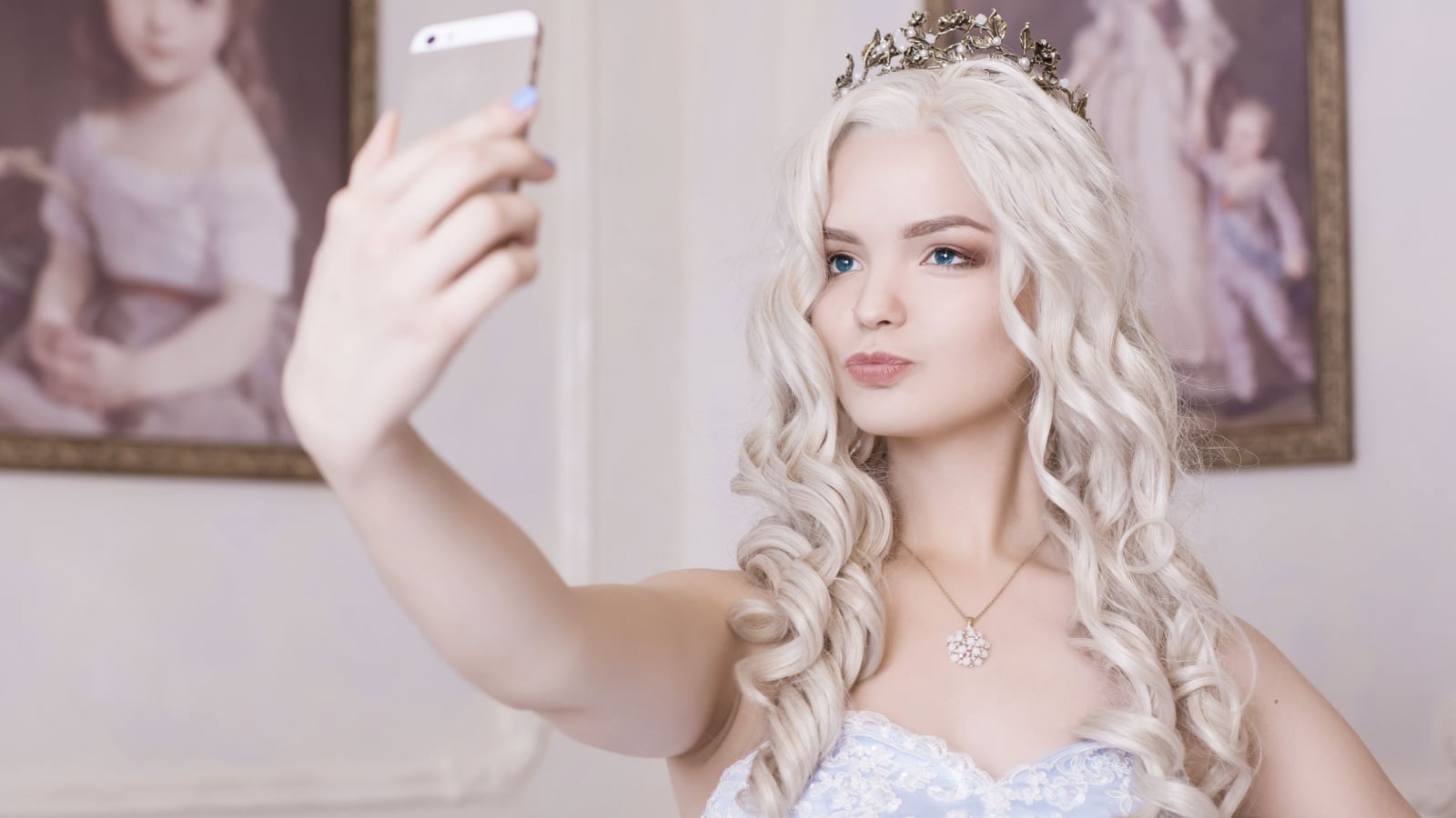 A pretty young woman is self obsessed. She's wearing a crown and taking a selfie to represent a spoiled brat.