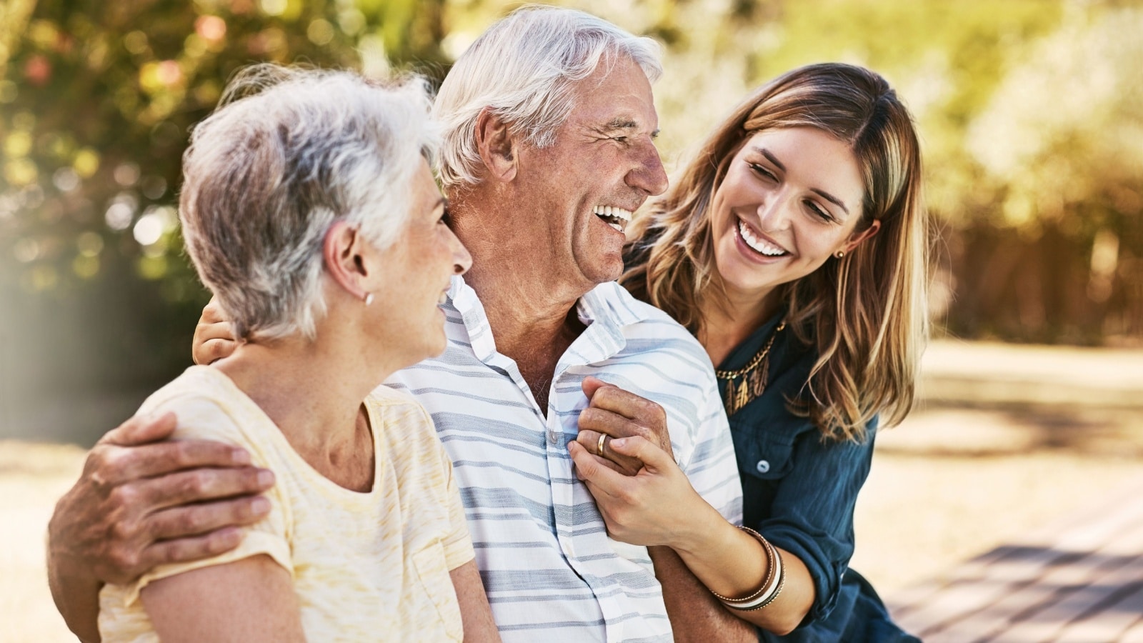 An adult daughter laughs with her senior parents outside.