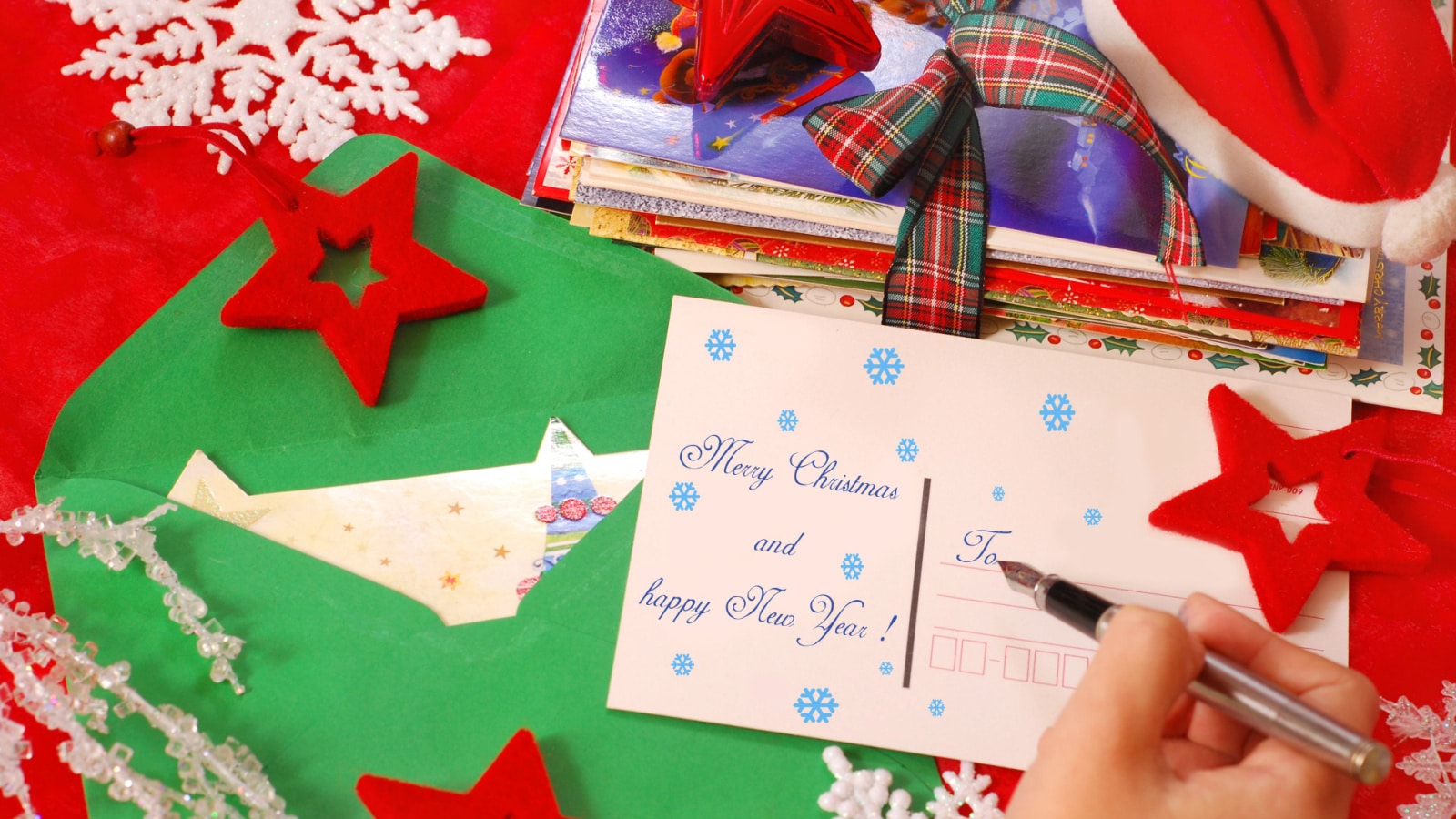 A stack of Christmas cards on a craft table with hands writing a personalized card.
