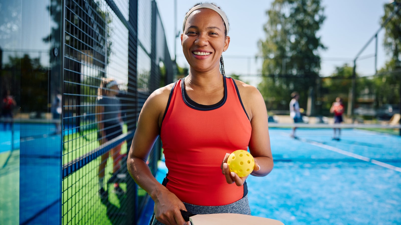 A smiling woman holds a pickleball and paddle on the court.