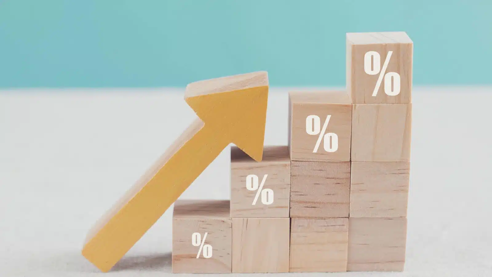 Wooden blocks stacked in a little staircase with the top of each block having a little percentage sign on it. An arrow rests on the staircase pointing up. 