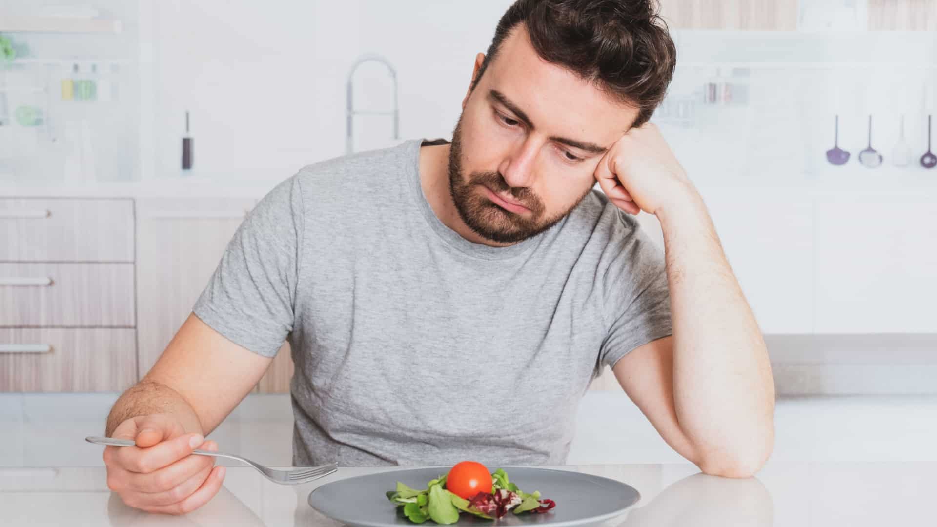 A sad man looks at his plate with hardly any food on it. It has a few lettuce leaves and a small tomato.