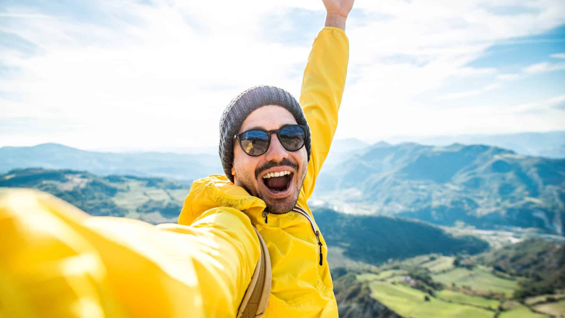 A happy traveler taking a selfie after hiking a mountain to represent safe travels.