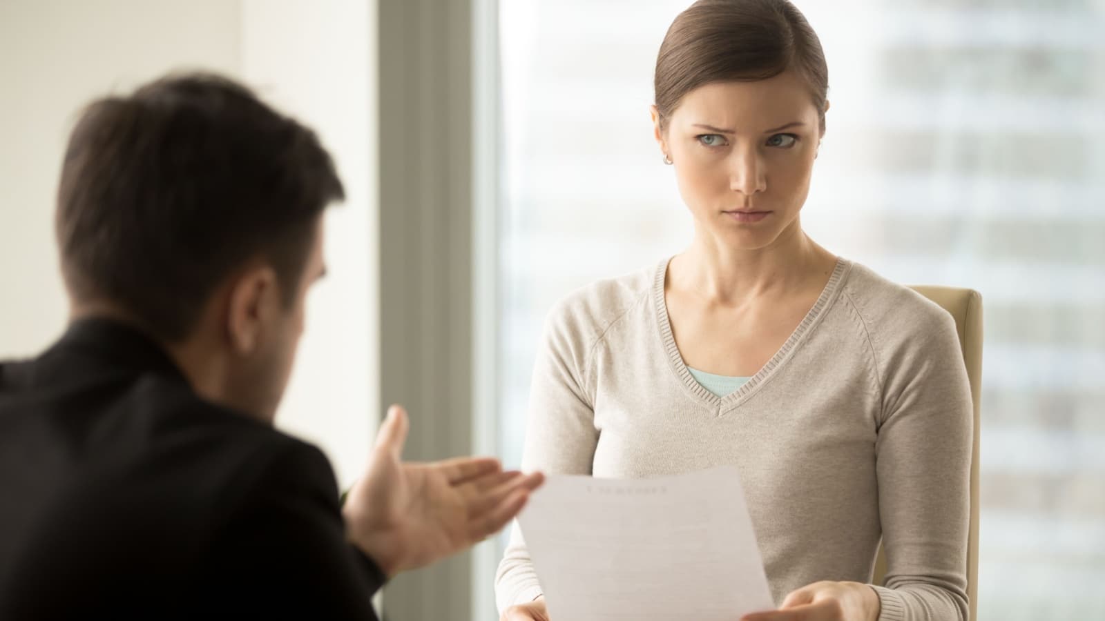 A woman look at a man skeptically as she's reviewing a paper he submitted.