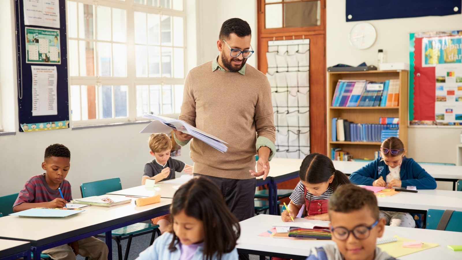 A teacher walking through his primary school classroom, checking the students' work.