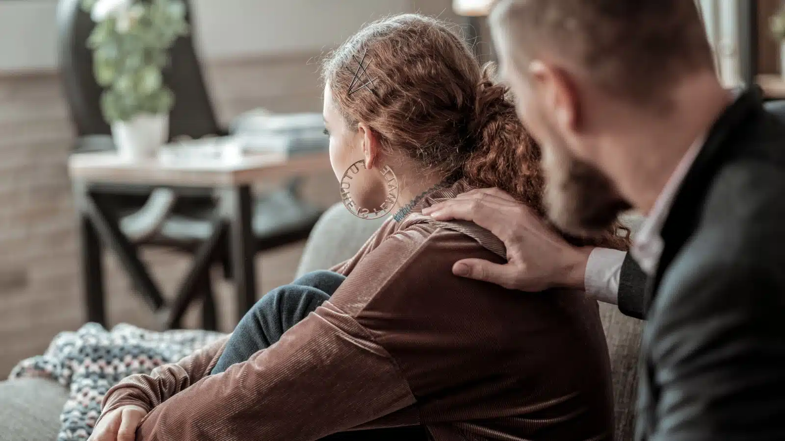 A male therapist has his hand on a female patient's shoulder as her back is turned.