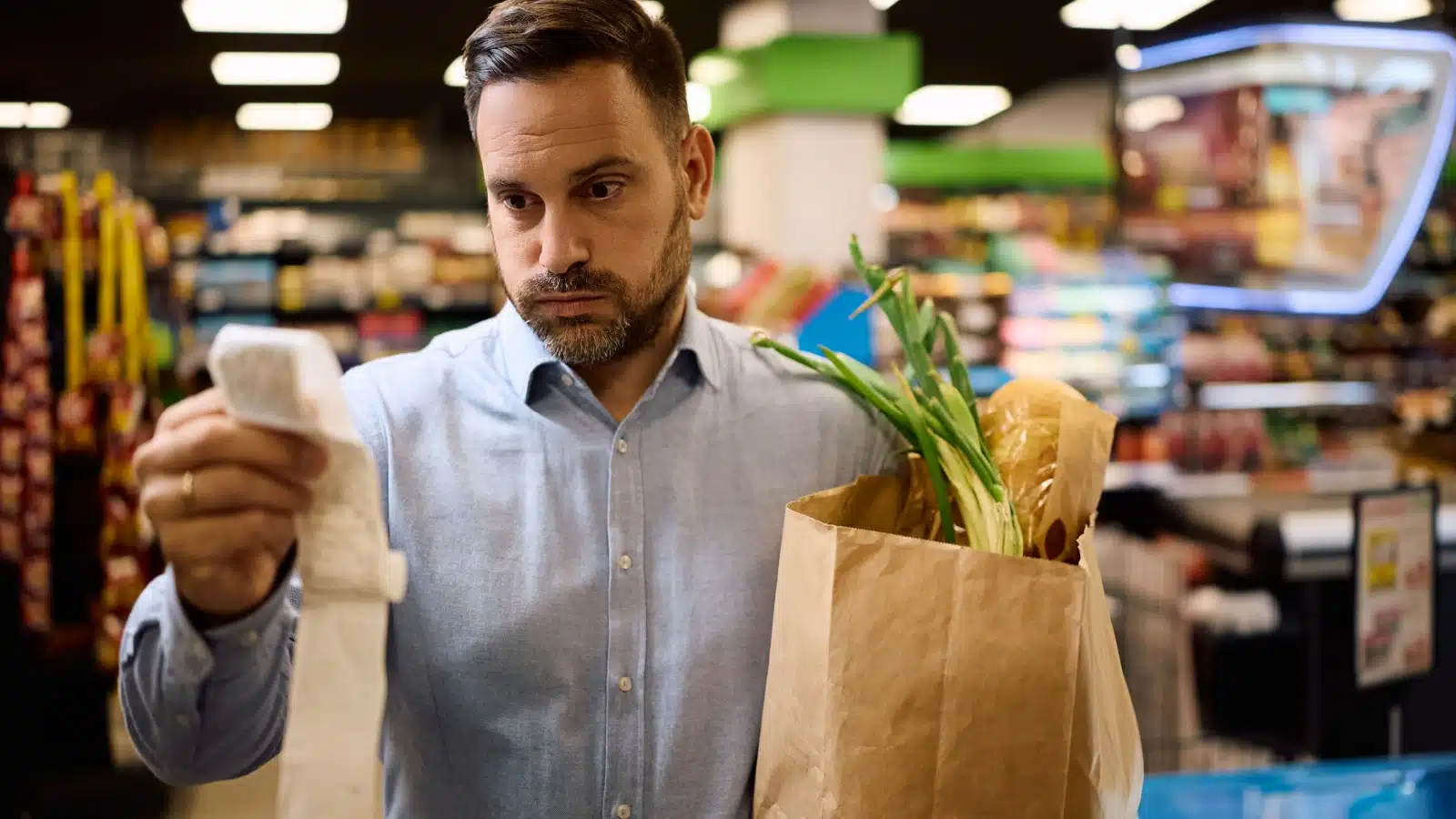A worried man looks at his grocery receipt, to represent things getting more expensive.