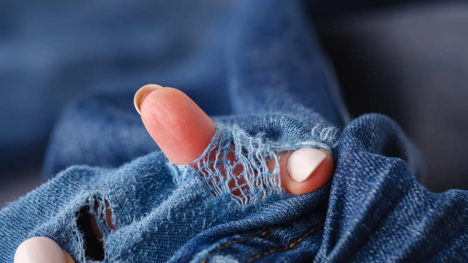 Fingers poking through a hole in cloth to show the poor quality. 