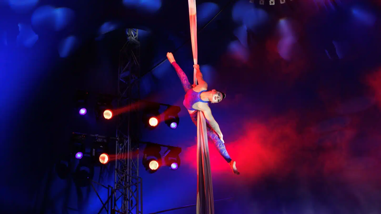 An acrobat hangs from a curtain during a performance.